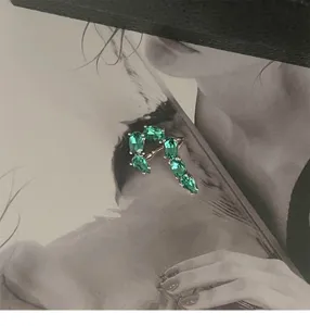 Macro view of French style J-shaped ear cuff featuring vivid green pear-cut zircons.