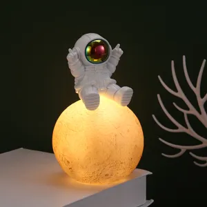 Statuetta astronauta seduta su lampada luna luminosa per l'arredamento della camera.
