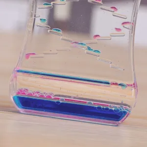Gros plan d'un sablier liquide bicolore montrant des gouttes d'huile roses et bleues