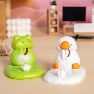 Gros plan de supports de téléphone en résine grenouille et canard sur un bureau miniature.