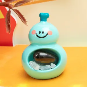 Gros plan d'une figurine de gourde bleu menthe avec un visage souriant et des pierres