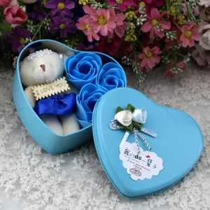 Close-up of a blue heart-shaped metal gift box containing 3 soap roses and a small white bear