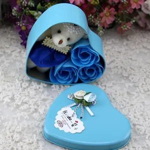 Detail view of a romantic heart-shaped blue tin box containing soap roses and a plush bear.