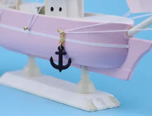 Detail of a black anchor charm hanging on a pink Mediterranean wooden sailboat model.