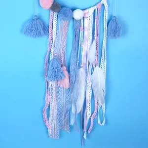 Handgemaakt dromenvanger detail met pluche pompons, kantlinten en zachte witte veren in pastel.