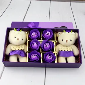 Gros plan d'un coffret cadeau avec deux ours en peluche et six roses de savon violettes