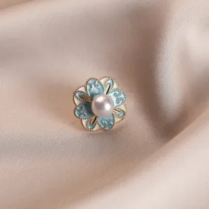 Close-up macro view of an elegant flower brooch with a pearl center on silk fabric background.