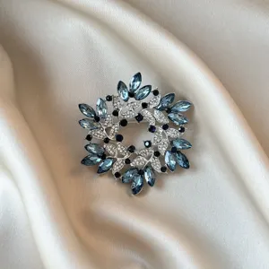 Detailed macro view of an elegant silver floral wreath brooch with blue marquise crystals