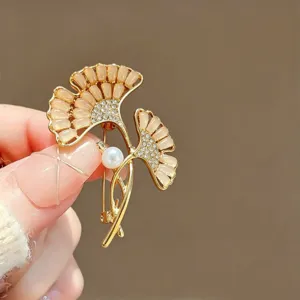Close-up detail of elegant ginkgo leaf brooch, shimmering rhinestones, pearl, gold tone.
