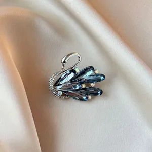 Close-up of elegant swan brooch with blue crystals and rhinestones on satin background.