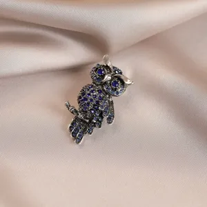 Close-up of a vintage style owl brooch sparkling with blue crystals on satin background.