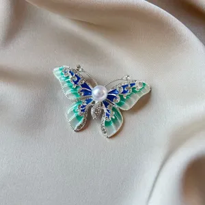 Detailed view of vintage butterfly brooch with green enamel and pearl centerpiece