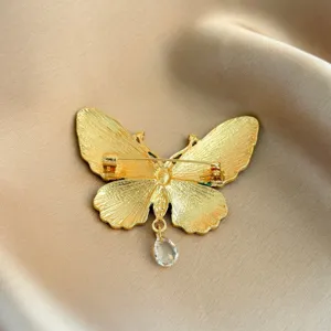 Detailed back view of golden butterfly brooch with elegant crystal teardrop pendant