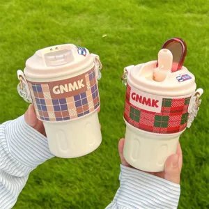 Detail of two portable insulated coffee mugs with plaid sleeves and straps in a grassy setting