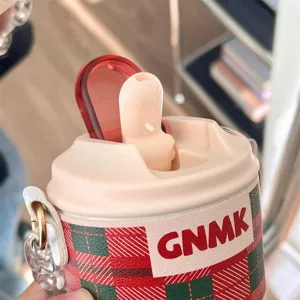 Close-up view of insulated coffee cup with red and green plaid sleeve and flip lid