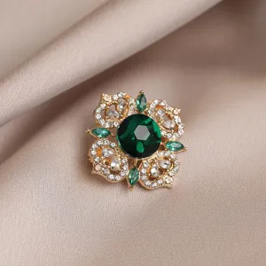 Detailed close-up of emerald green crystal flower brooch with sparkling clear stones.