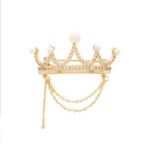 Close-up of a gold-plated crown brooch featuring glittering rhinestones and delicate hanging chains.