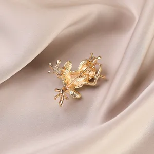 Gold frog brooch detail view, metal alloy lapel pin accessory, elegant clothing decor.