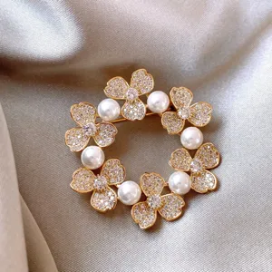 Elegant gold wreath brooch close-up featuring sparkling rhinestones and pearls for chic outfit decor.