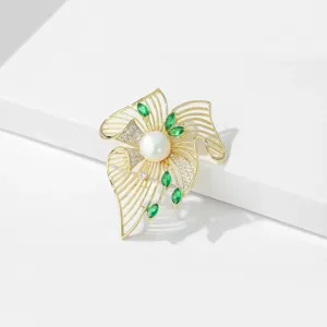 Close-up view of elegant gold-toned filigree brooch featuring glowing pearl and vibrant green gems.