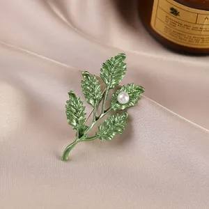 Close-up detail of an elegant green leaf brooch featuring a shimmering white pearl accent