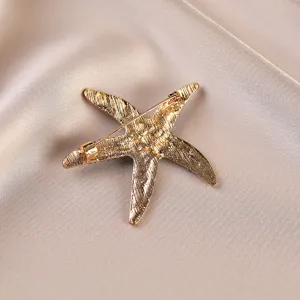 Close-up detail view of the back side of a gold-toned starfish brooch pin with textured metal.