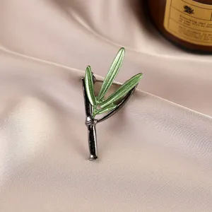 Close-up detail of a green bamboo leaf brooch with elegant metallic finish on silk