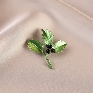 Macro view of elegant green holly leaf brooch featuring black berries on satin fabric