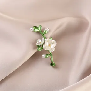 Elegant close-up of a white flower brooch with green leaves pinned on beige silk fabric.