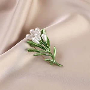 Elegant green plant brooch with white pearl droplets on soft silk fabric background