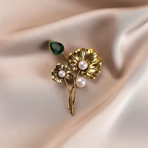 Macro view of vintage golden lotus leaf brooch with teardrop green crystal and pearls