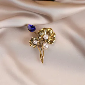 Detailed close-up of vintage gold lotus leaf brooch with blue crystal and pearls