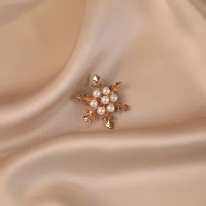 Detailed view of a gold-toned snowflake brooch featuring elegant white pearls on silk.