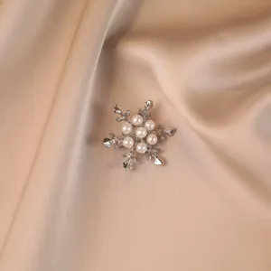 Close-up of snowflake-shaped silver brooch with elegant white pearls on champagne satin fabric