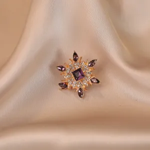 Close-up of a vintage gold-toned brooch with purple crystals on champagne silk background