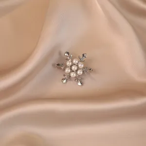 Detailed close-up of a silver snowflake pearl brooch on elegant champagne satin fabric