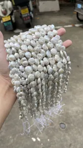 Close-up detail of a hand holding multiple strands of natural white Baroque pearls