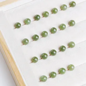 Macro close-up view of translucent green natural Hetian jade round beads on white tray