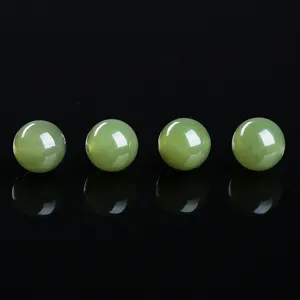 Detailed view of four natural green Hetian jade beads on black reflective surface