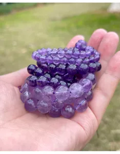 Close-up of various sized natural amethyst beads held in hand against outdoor background