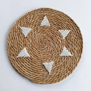 Macro view showing the intricate texture of round straw woven placemat with white embroidery