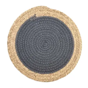 Top-down view of a round woven placemat featuring dark grey cotton and natural straw.