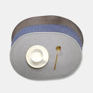Vue détaillée de sets de table ovales tissés en PP nordique avec surface texturée et une tasse.