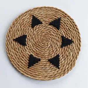 Top-down view of a round woven straw placemat with black triangular patterns