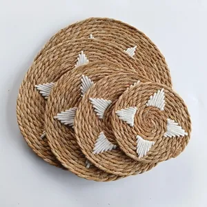 Set of stacked round straw woven placemats with white geometric embroidery patterns
