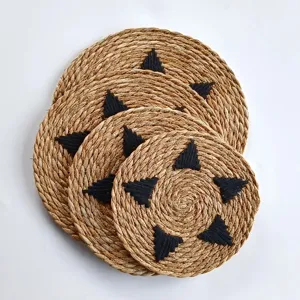 Macro view of handcrafted seagrass placemat with black triangular embroidery detail.