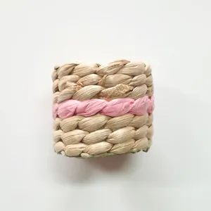 Dettaglio portatovagliolo intrecciato, paglia naturale con accento treccia rosa tavola.