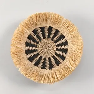 Detail of bohemian round straw wall hanging with black woven pattern and natural raffia fringe.