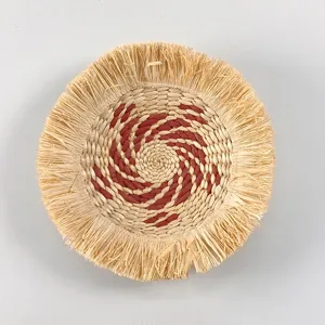 Handmade straw woven wall hanging detail featuring red spiral pattern and textured raffia fringe.