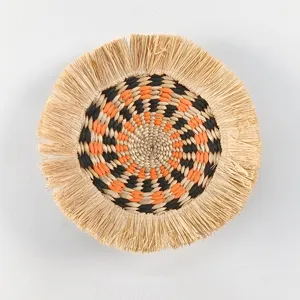 Detail of bohemian straw wall hanging, featuring raffia fringe and geometric spiral design.